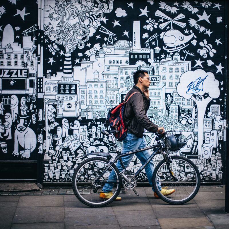 Man walking bike with basket by graffiti