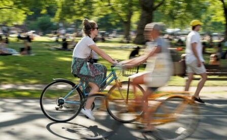 Woman on yellow bike cycling through park in sunshine