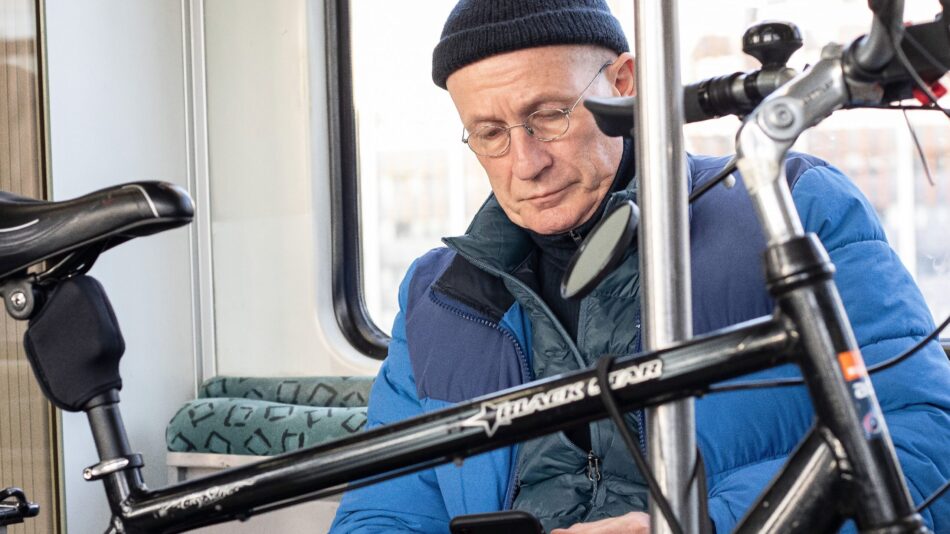 A man looking at his phone while taking a bike on the train