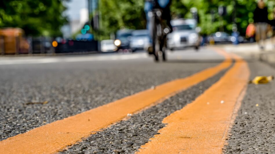 Low view of a cyclist riding beside double yellow lines on road with traffic